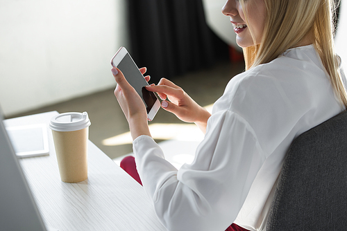 cropped shot of smiling young woman using smartphone at workplace