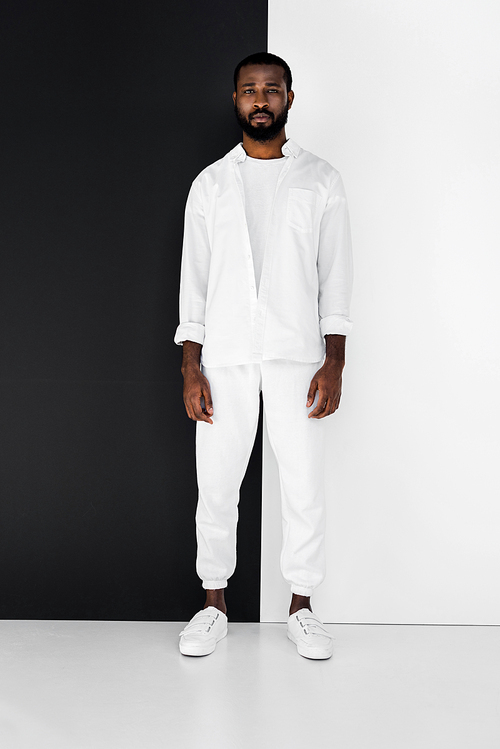 handsome stylish african american man in white clothes near black and white wall