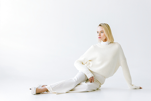 beautiful stylish blonde woman in white clothes sitting on white floor and looking away