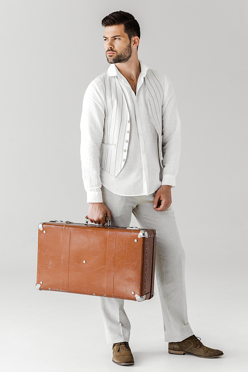 serious stylish male traveler in linen clothes holding vintage suitcase isolated on grey background