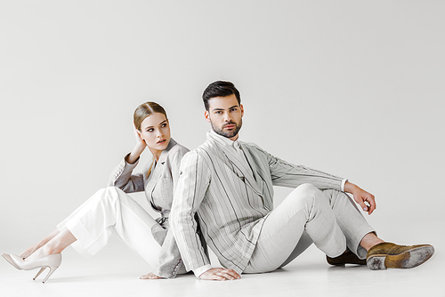 couple of attractive models in vintage clothes sitting on floor and leaning back to back on white