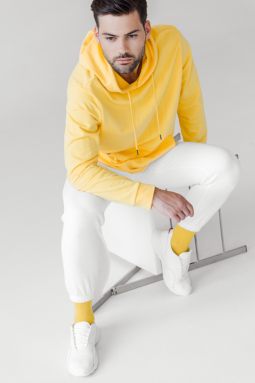 high angle view of handsome young man in yellow hoodie sitting on flipped chair on white