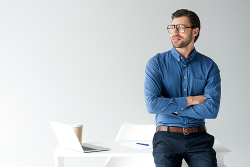 handsome young businessman with crossed arms leaning back at workplace isolated on white