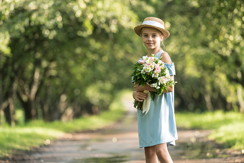 beautiful child in dress and straw hat with flowers standing in park