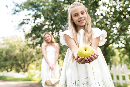 preteen daughter holding apple, young mother with wicker basket on background, selective focus