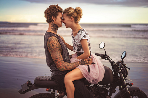 happy couple hugging and touching with foreheads on motorcycle on ocean beach