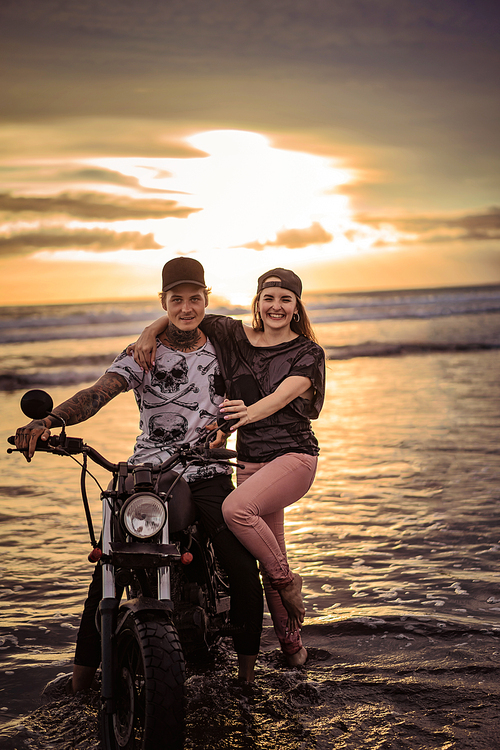 smiling couple with motorcycle on ocean beach