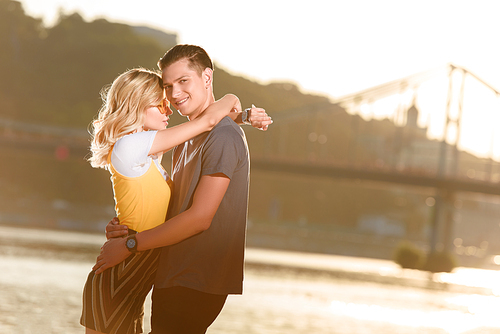 side view of young couple hugging on river beach in evening