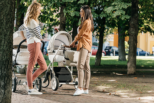 side view of mothers talking and standing with baby strollers in park