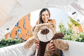 smiling mother holding teddy bear in baby stroller