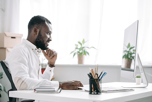 side view of cheerful handsome african american businessman working at computer in office