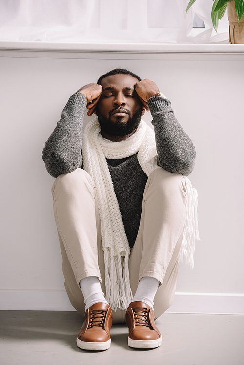 tired ill african american man in white scarf sitting on floor