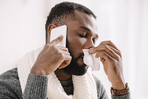 diseased african american man with runny nose holding napkin while talking on smartphone