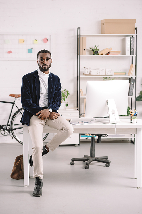 stylish african american businessman leaning on table with computer in modern office