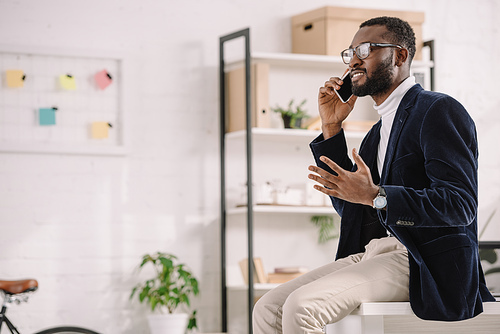 bearded african american businessman talking smartphone on while sitting on table in modern office