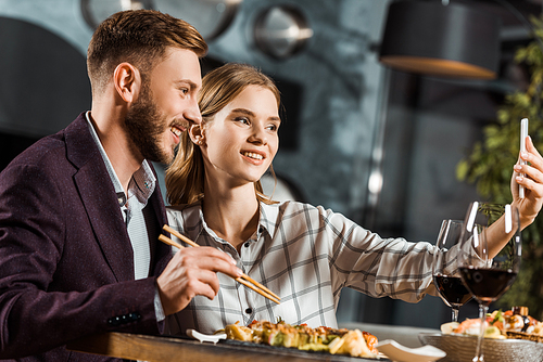 Side view of attractive couple taking selfie during dinner in restaurant