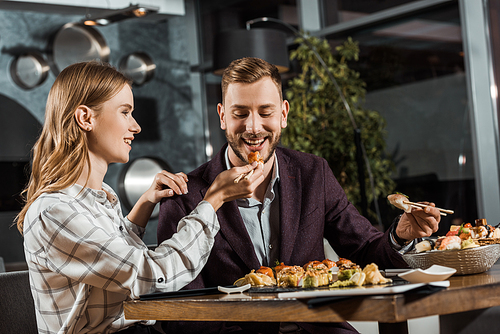 Attractive young adult woman feeding her handsome boyfriend in restaurant