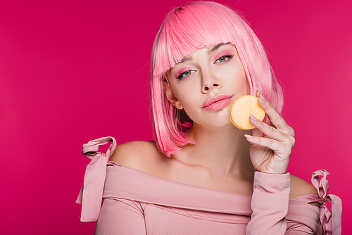 beautiful woman in pink wig posing with macaron isolated on pink