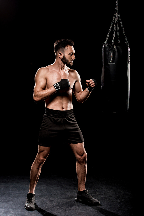 handsome boxer kicking boxer bag on black background