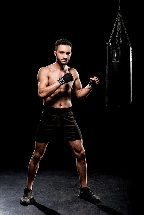 handsome boxer  near boxer bag on black background