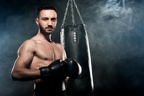 handsome athlete standing in boxing pose on black with smoke