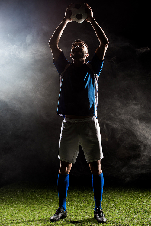 silhouette of football player holding ball above head on black with smoke
