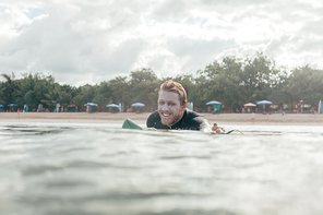 smiling surfer lying on surf board in ocean, beach on background