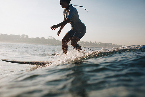 silhouette of sportswoman surfing in ocean, coastline on background