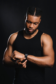 handsome serious african american sportsman using smartwatch isolated on black