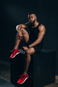 full length view of muscular young african american man in sportswear sitting on black