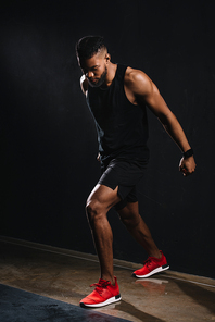 full length view of muscular young african american man in sportswear exercising on black