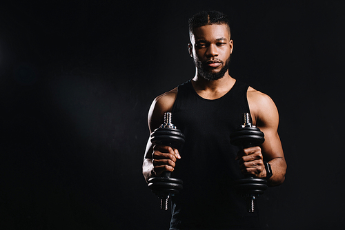 muscular young african american sportsman holding dumbbells and  isolated on black