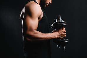 cropped shot of muscular young sportsman training with dumbbells isolated on black