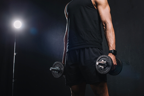 cropped shot of young african american sportsman holding dumbbells on black