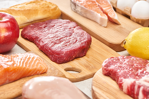 Fresh raw meat, fish, poultry on wooden cutting boards near apple, lemon, baguette and eggs