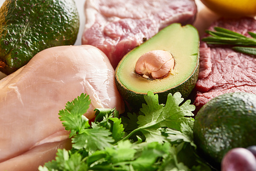 Close up view of half of avocado between raw meat and poultry with parsley twigs