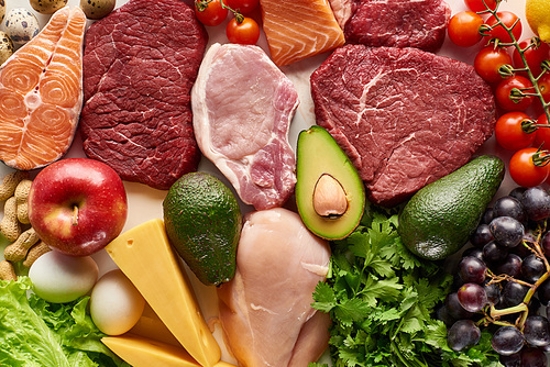 top view of assorted raw meat, poultry, fish, eggs, s, fruits, nuts, greenery and cheese