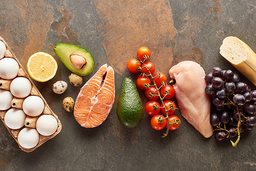 Top view of raw fish and poultry near vegetables, fruits, eggs and baguette on marble surface with copy space