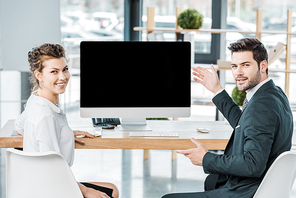 young smiling business colleagues at workplace with blank computer screen in office