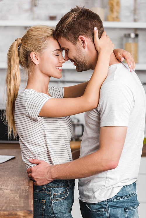 side view of happy couple hugging in kitchen