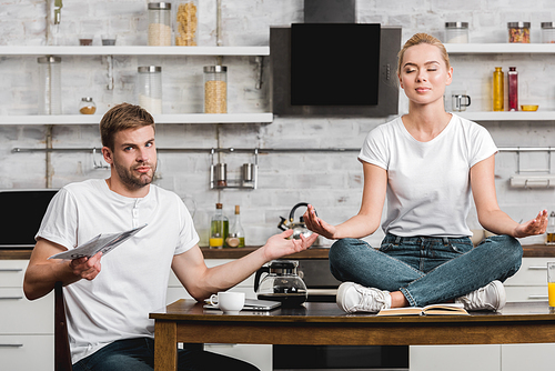 young man holding newspaper and  while beautiful girlfriend meditating on kitchen table