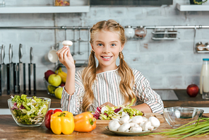 beautiful little child with mushroom and various raw vegetables  while making salad at kitchen