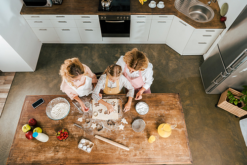top view of child with mother and grandmother cutting dough for christmas cookies at home