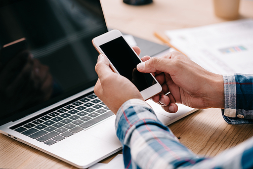 cropped shot of businessman using smartphone at workplace with laptop