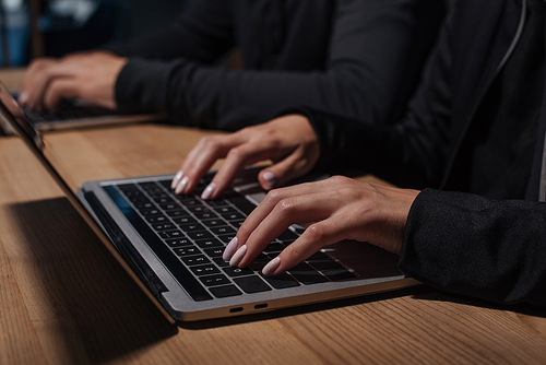 cropped shot of hackers using laptops at wooden tabletop, cyber security concept