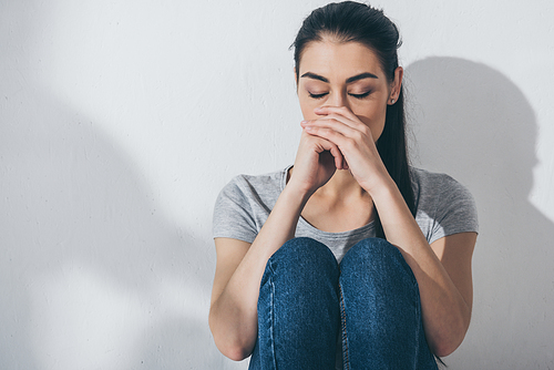 sad stressed girl sitting with closed eyes near grey wall