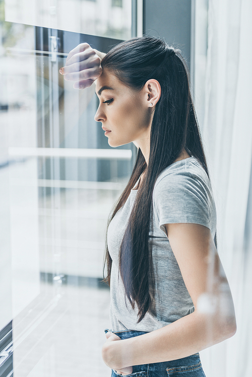 side view of upset young woman leaning at window and looking down