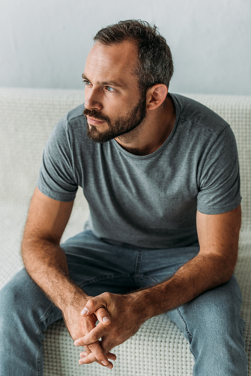 bearded thoughtful middle aged man sitting on couch and looking away