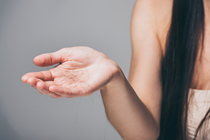 cropped shot of young woman holding fallen hair in hand isolated on grey, hair loss concept
