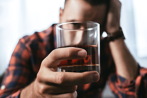 close-up shot of depressed man holding glass of whiskey